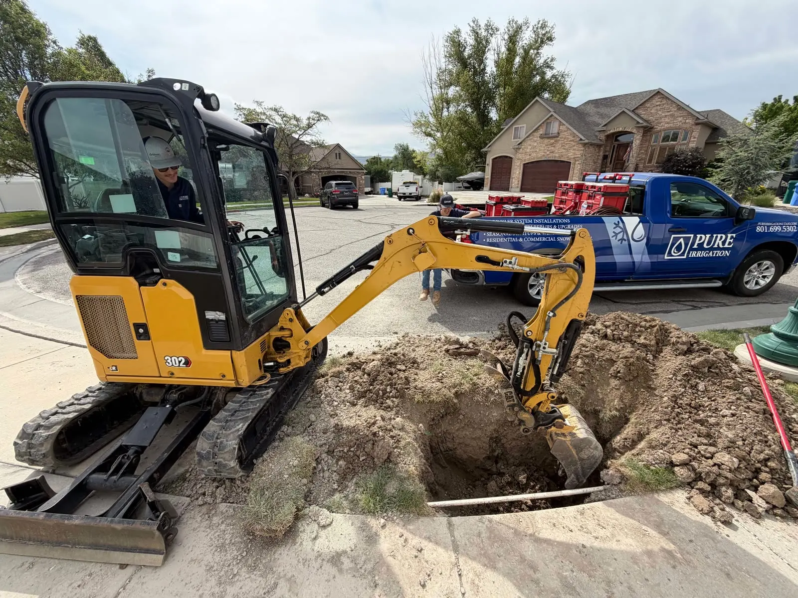 Pure Irrigation technicians using a mini-excavator next to their branded truck on a residential job