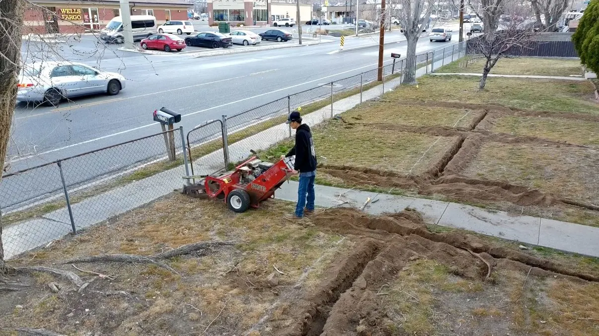 A Pure Irrigation technician running a trencher to install new irrigation lines across a yard